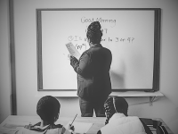Photo of female teacher writing on white board with two pupils in the front row.